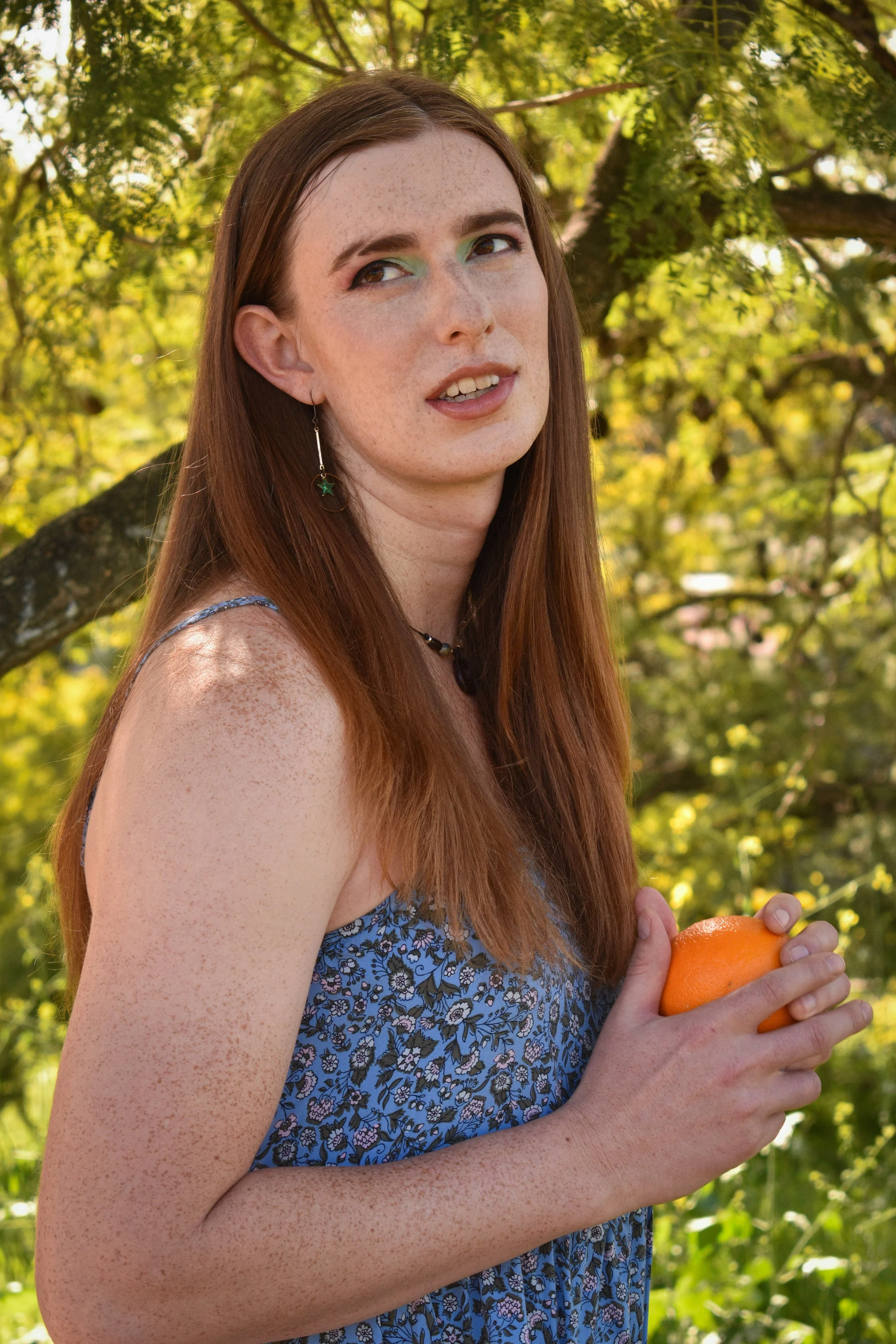 Person in blue dress holds orange and looks wistful