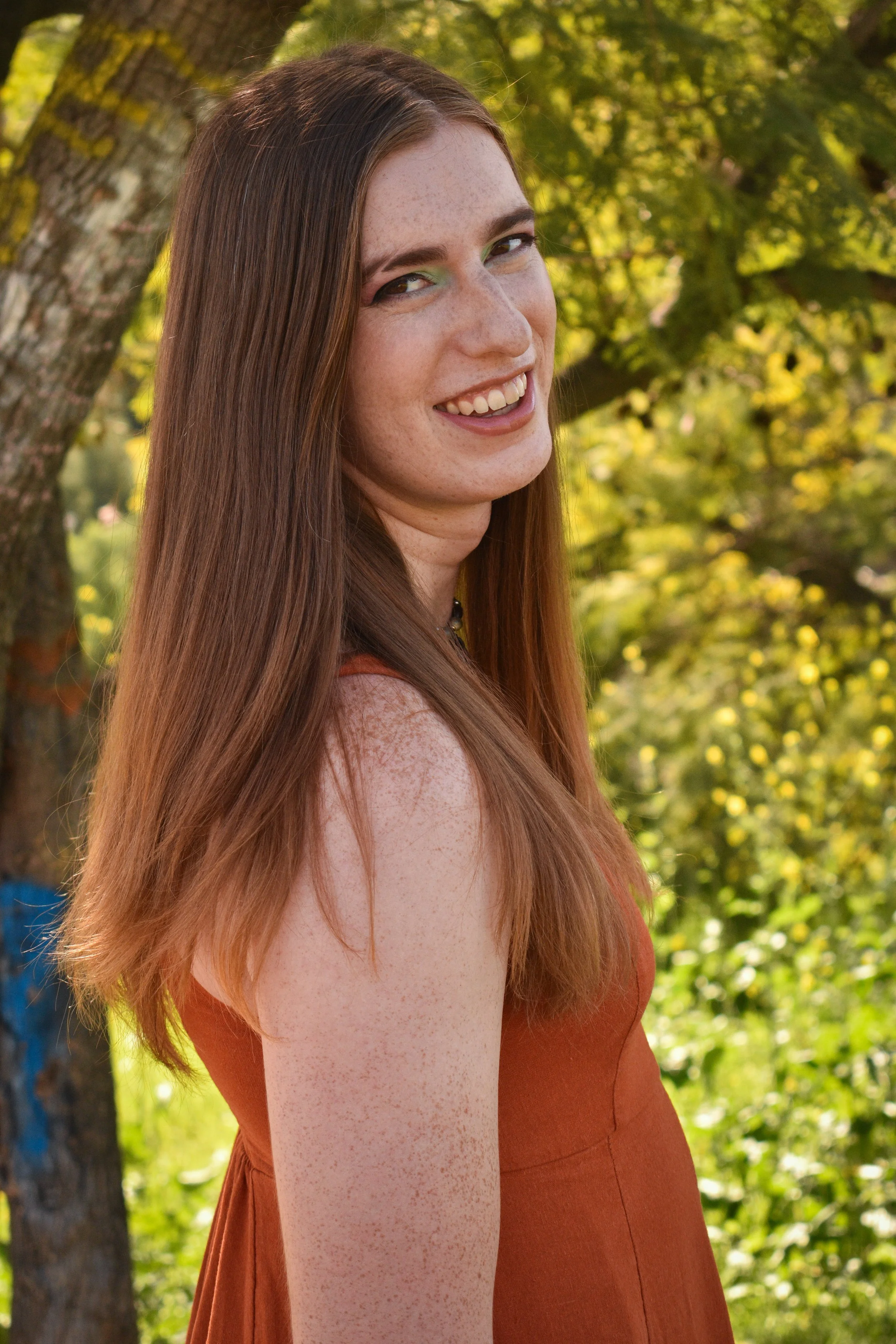 Person in orange dress stands under tree and smiles
