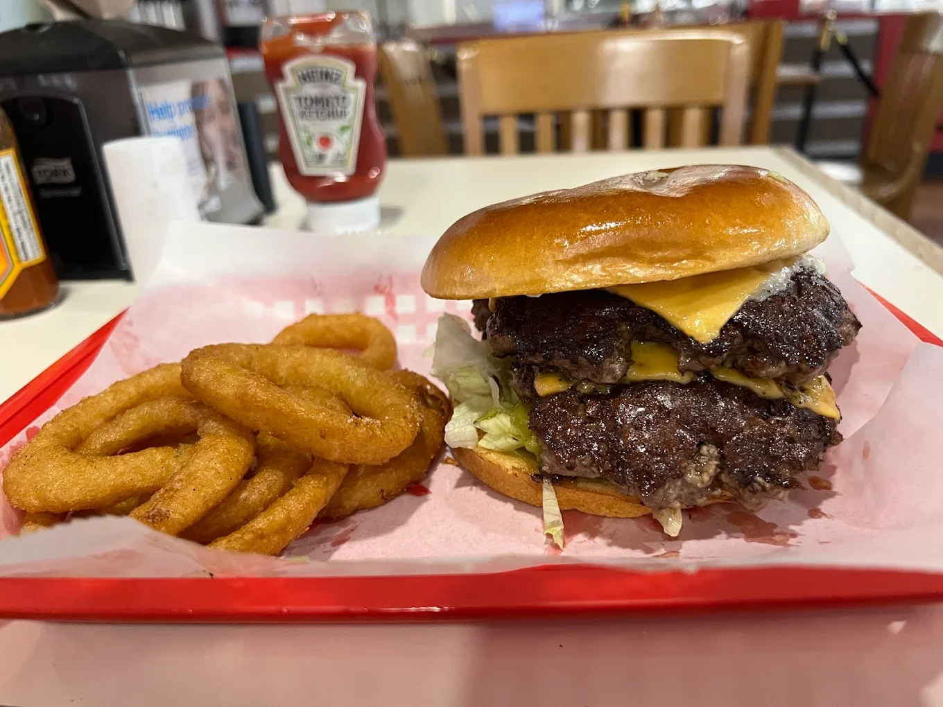A cheeseburger with two beef patties, melted cheese, lettuce, and a bun, served with curly fries on a red tray.