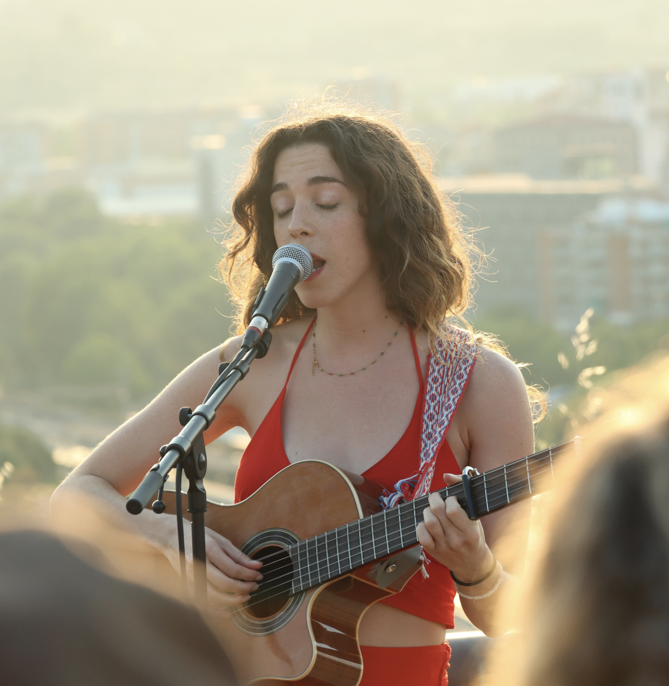 Claudia Bloom cantando y tocando la guitarra acústica en un concierto al atardecer.