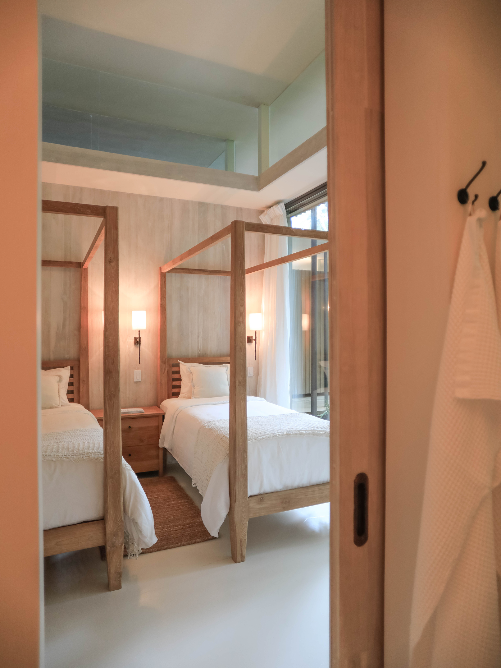 Room with two beds, wooden headboards, nightstands, lamps, and a window, reflected in a mirror door.