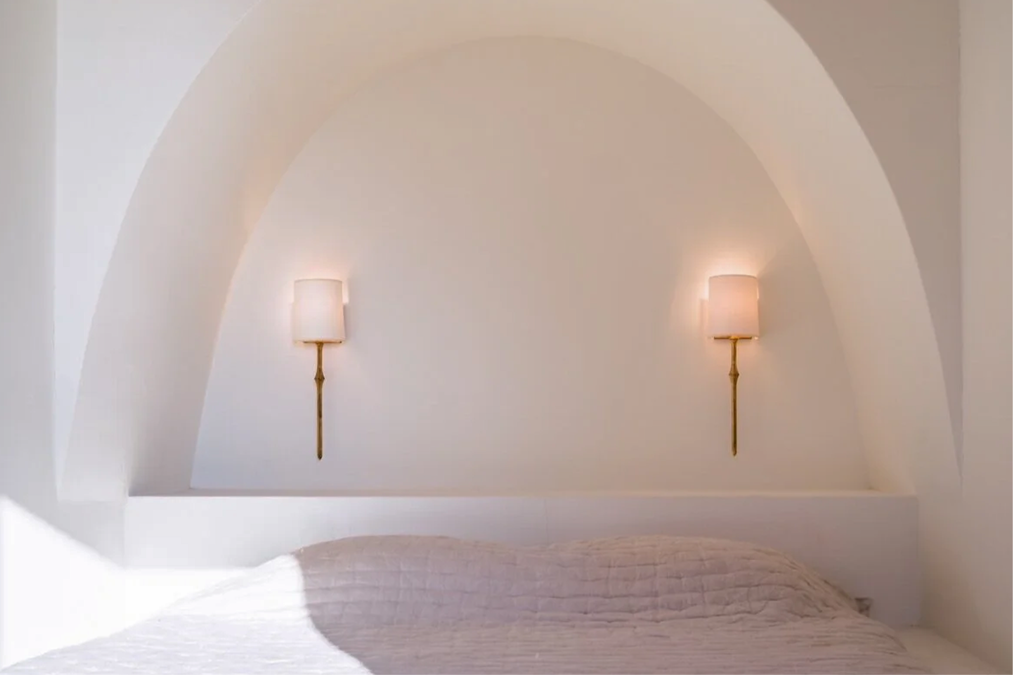 A bedroom with a vaulted ceiling, two wall-mounted lamps, and a bed with a beige quilted blanket.