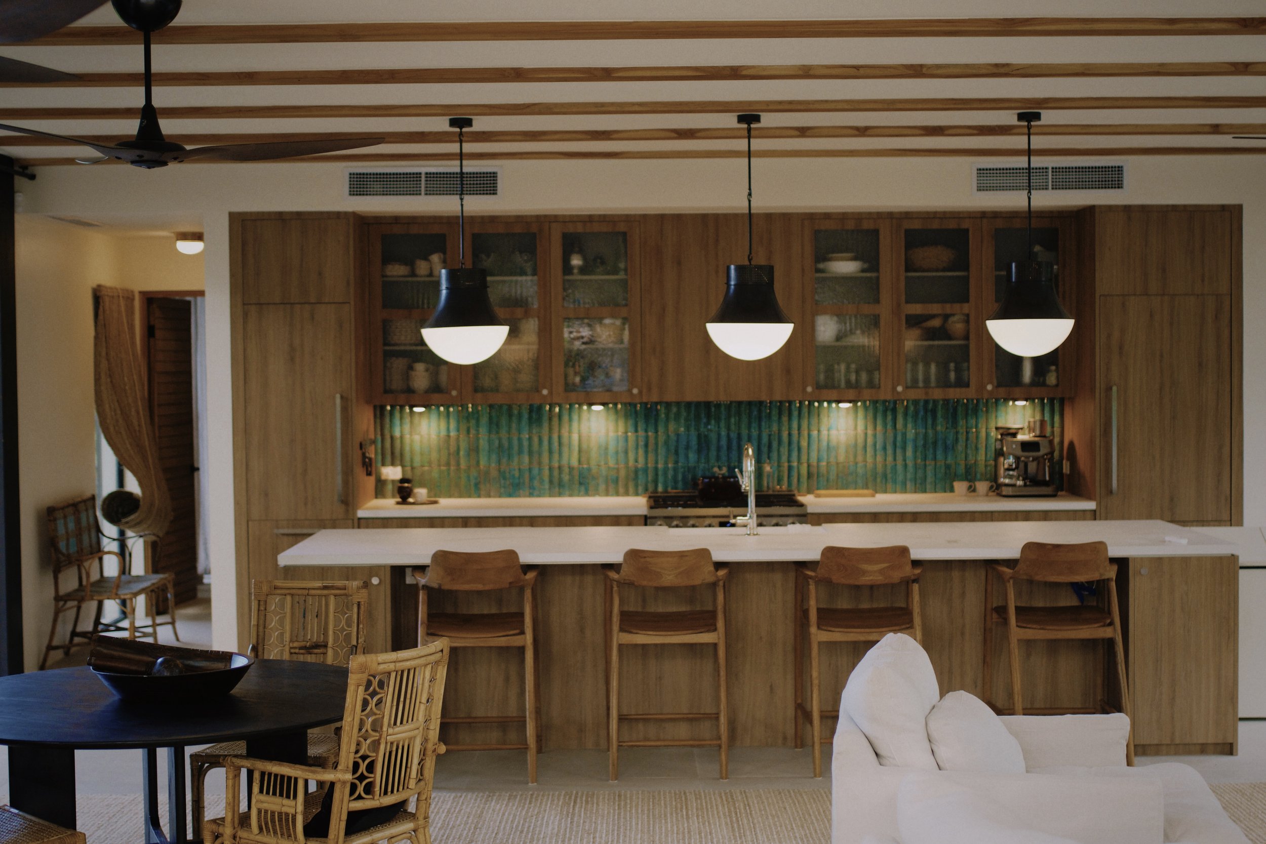 Modern kitchen with wooden cabinets, glass-front upper cabinets, pendant lighting, and a kitchen island with chairs.