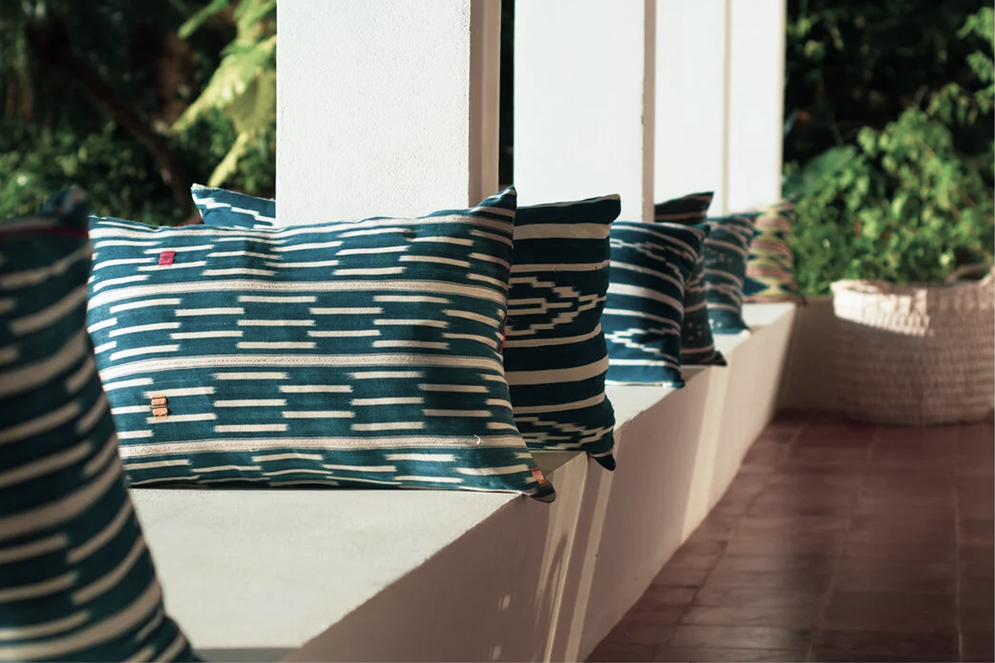 Line of navy blue and white striped pillows on a white wall ledge outdoors with greenery in the background.