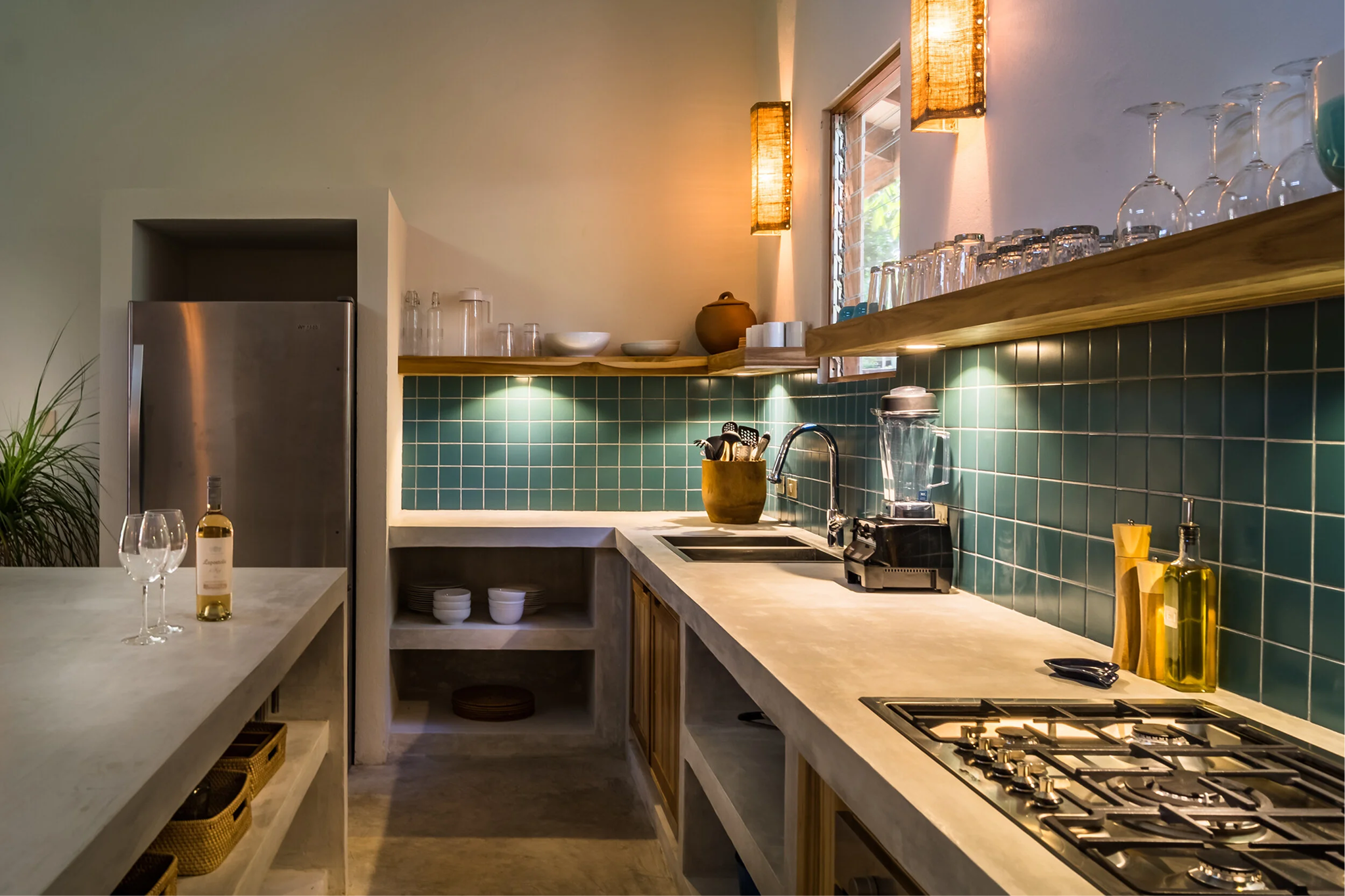 A modern kitchen with green tiled backsplash, wooden shelves with glassware, a refrigerator, and a marble countertop with wine glasses and a wine bottle.