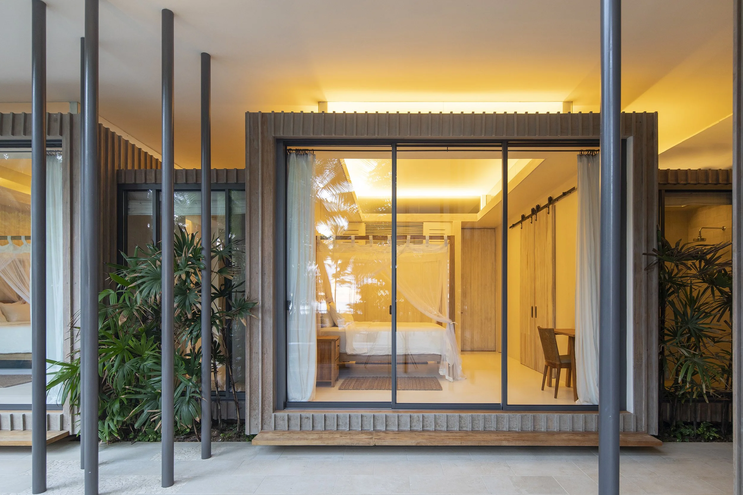 Modern house interior with a glass sliding door, curtains, plants, and warm lighting.