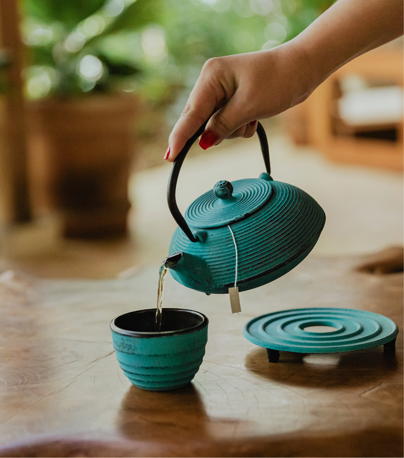A person is pouring tea from a blue teapot into a matching blue teacup on a wooden table.