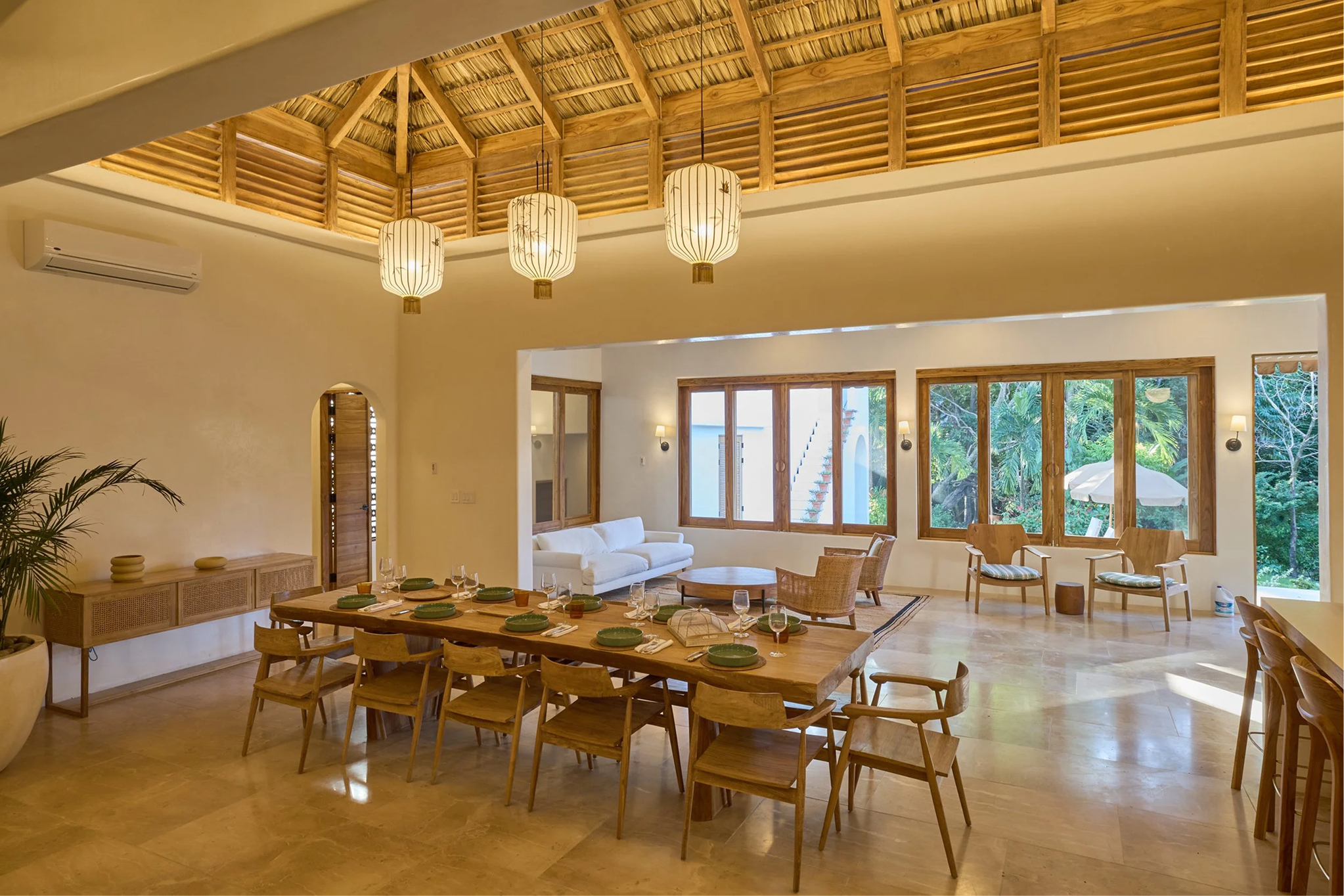 Bright, open living and dining room with high wooden ceiling, large windows, and tropical decor.