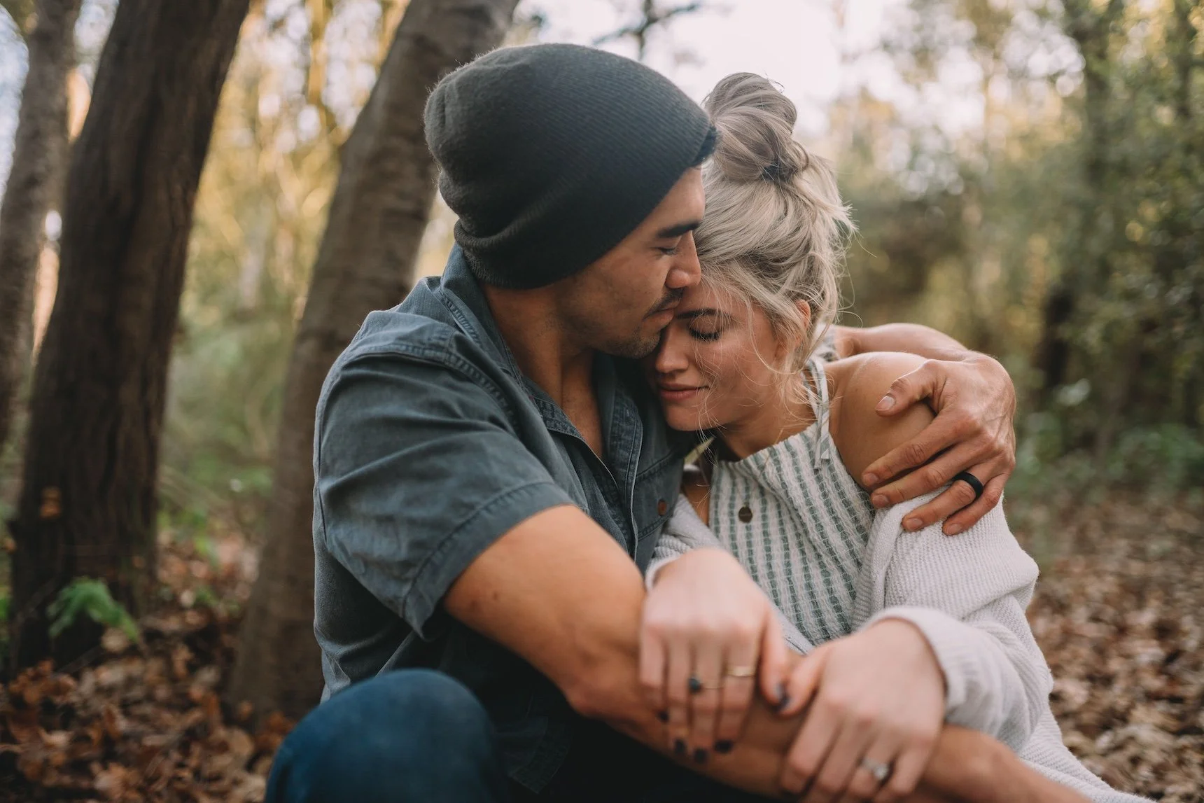 A man and woman embrace each other tenderly in a forest, with their eyes closed, conveying deep affection and connection.