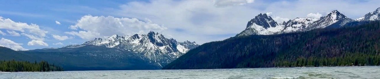 Snow-capped mountains overlooking a lake and forest in Idaho, reflecting themes of nomadic travel, nature, and freedom.