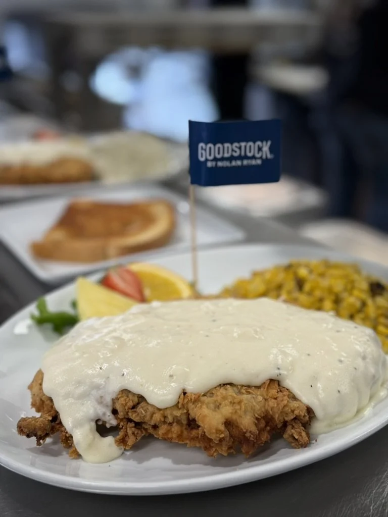 Plate of fried chicken with white gravy, side of corn, and fresh fruit, on a white plate with a small blue flag that reads "Goodstock by Hilton Detroit."