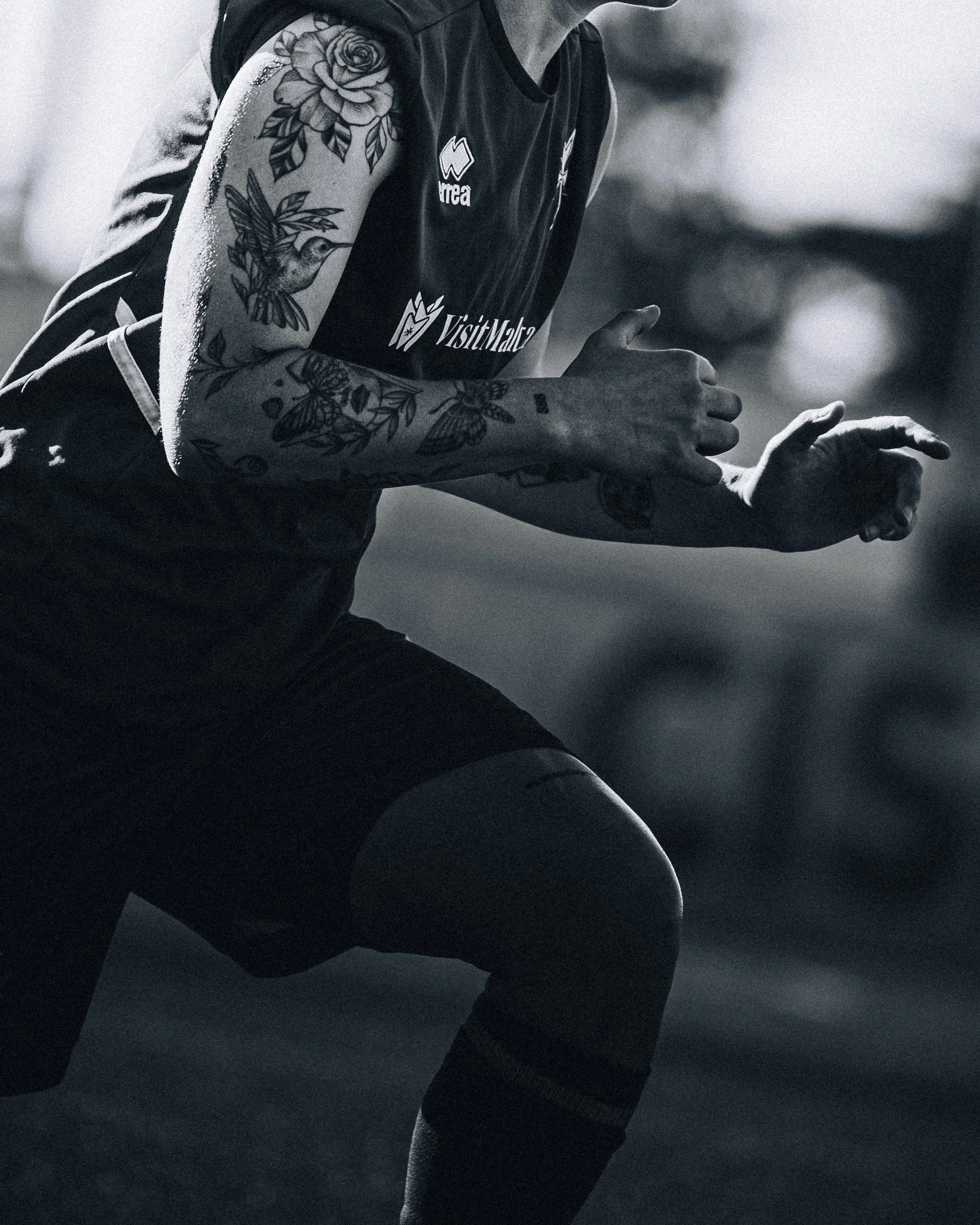 Close-up of a person with arm tattoos in a black sports jersey, captured in motion, in a dark environment.