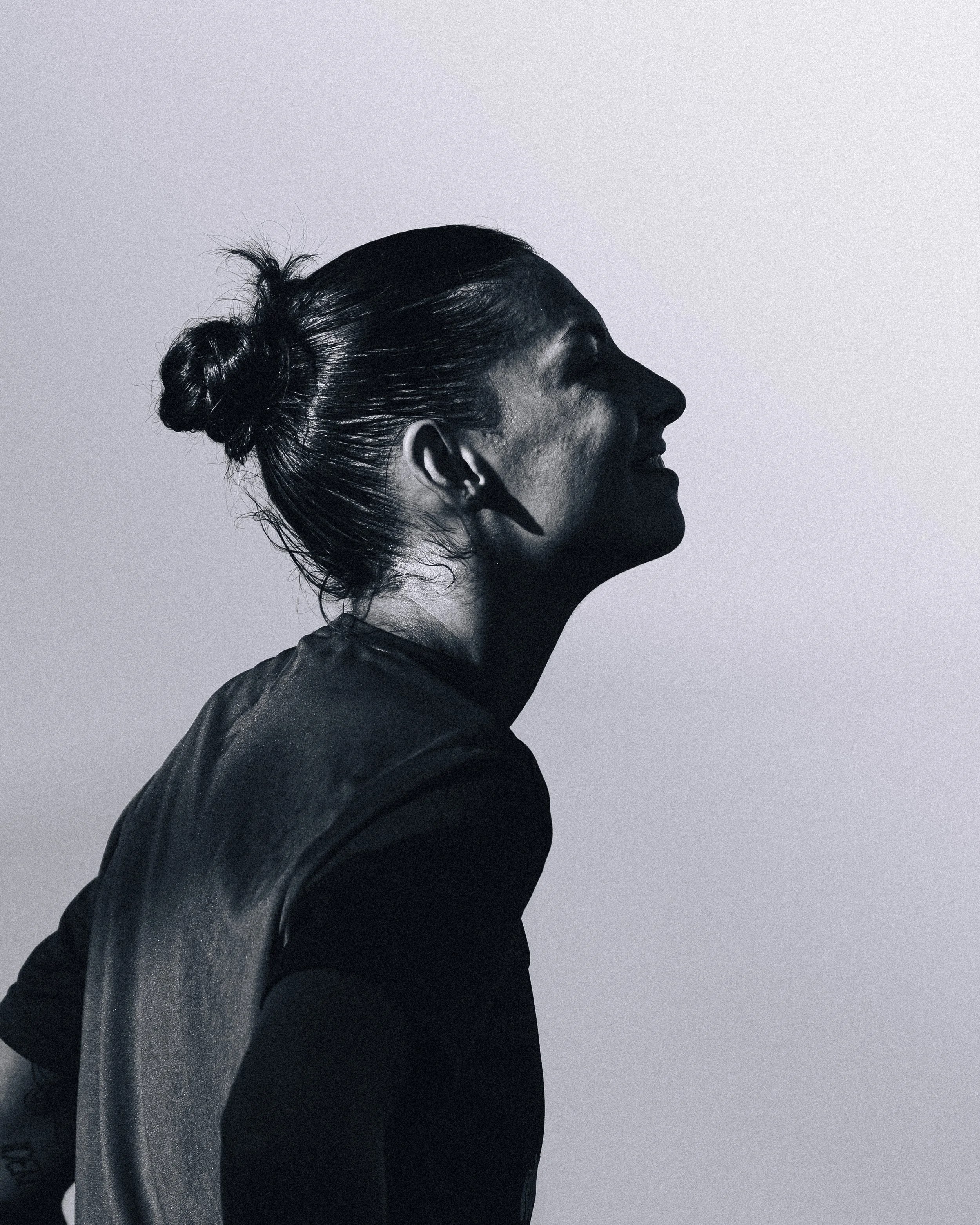 Black and white side profile of a woman with hair in a bun, wearing a dark top, against a plain, light background.