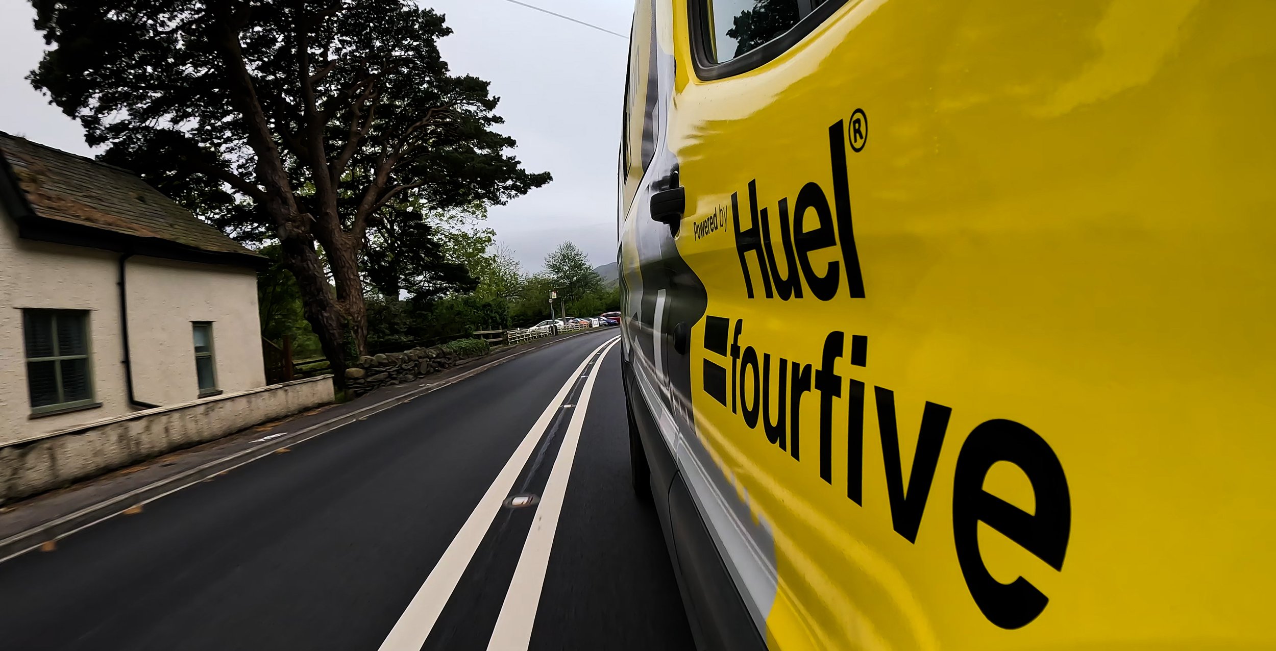 View of a winding street with a yellow vehicle, partially visible on the right side, displaying the text 'Powered by Hertz' and 'Tour'.