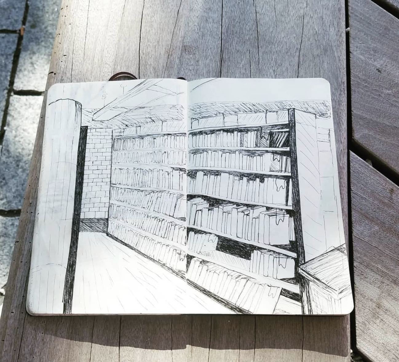 Black ink sketch of a bookshelf filled with books, located in a room with a brick wall and a wooden ceiling. Sarah Heyward's sketchbook documentation.