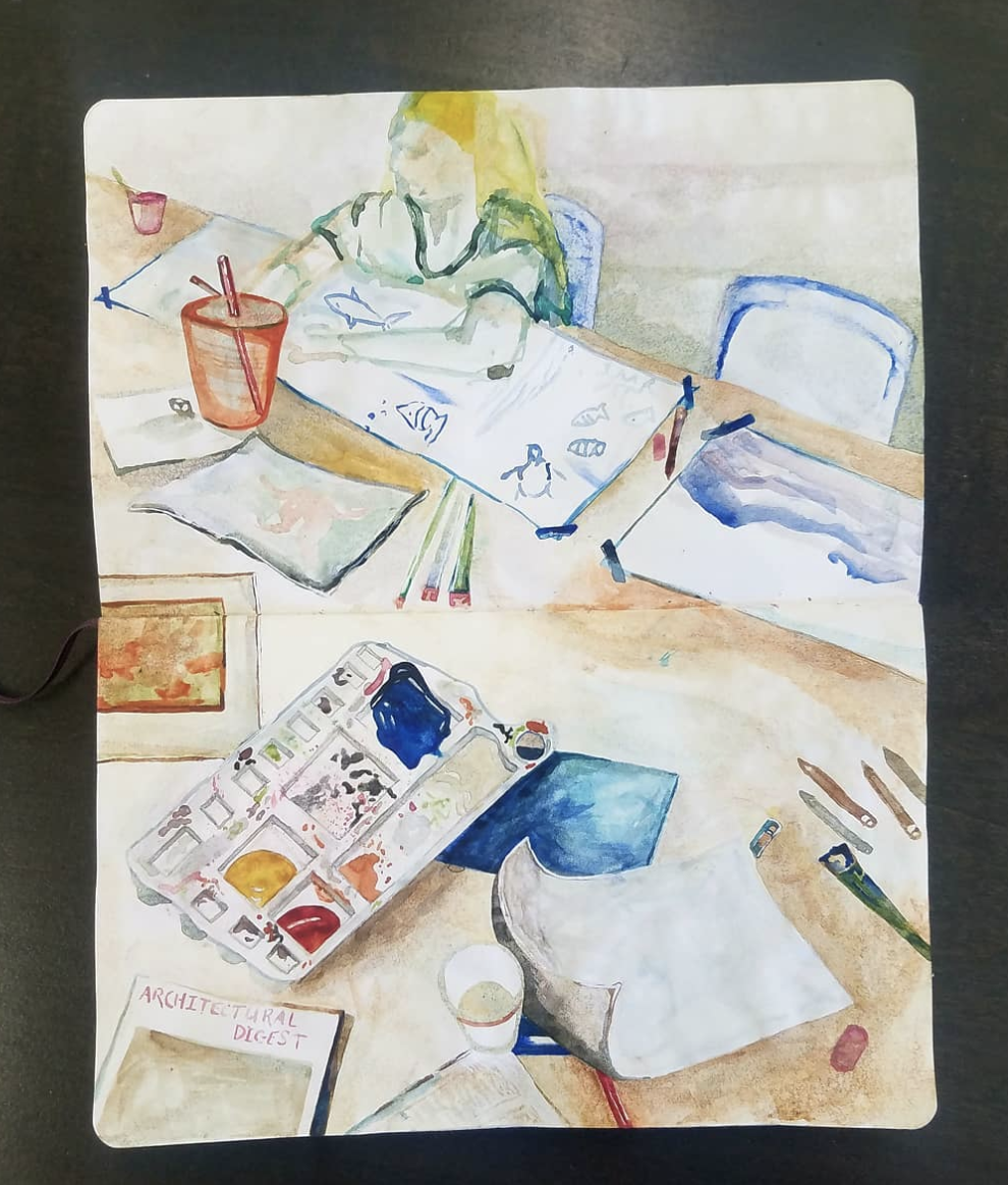 Watercolor painting of a workspace with a person drawing at a table. The table has art supplies including a palette, paper, pens, and brushes. A cup of coffee or tea is also present. The background shows a person in a green shirt with blonde hair wor