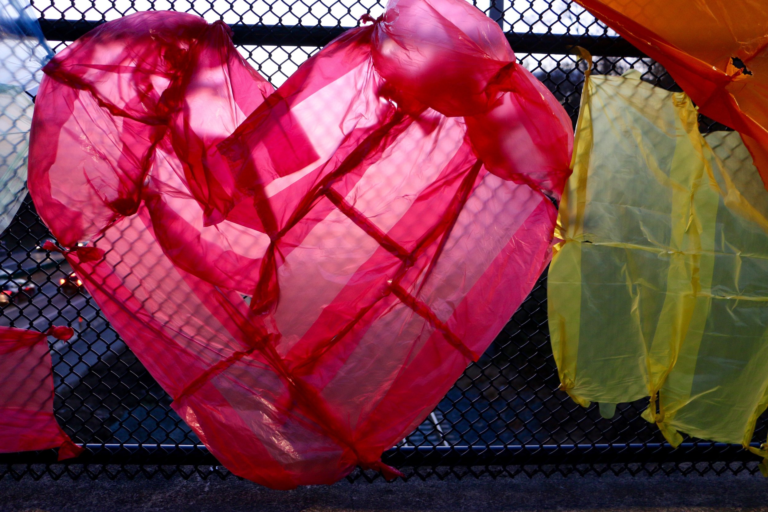 Colorful plastic bags hanging on a black metal fence.