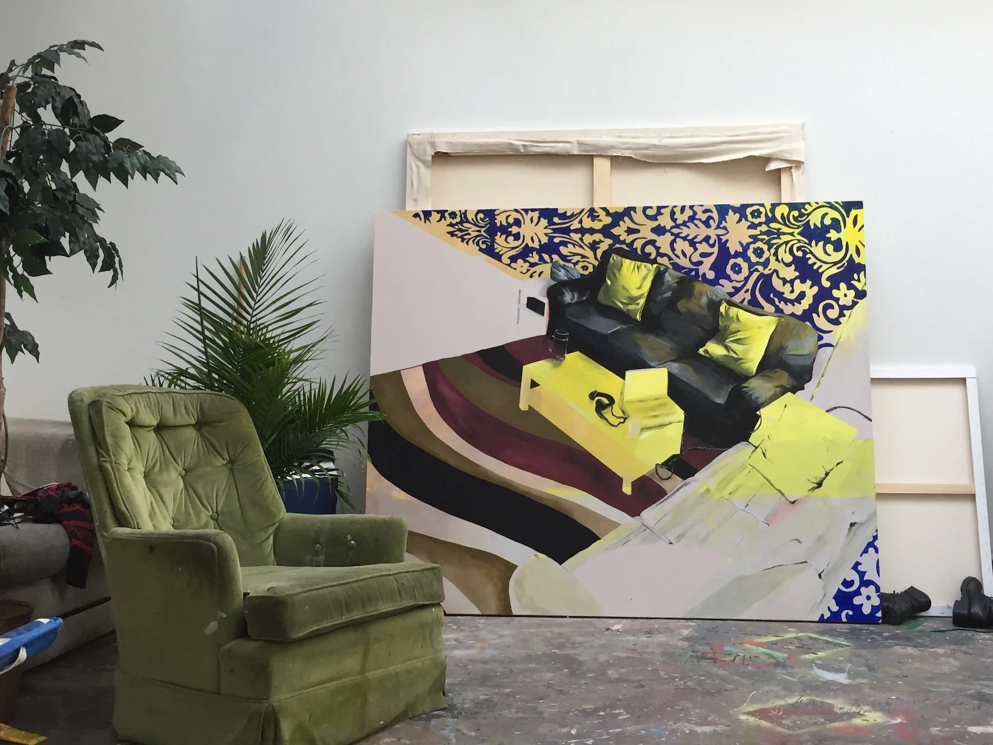 Painted artwork leaning against a wall in Sarah Heyward's studio, with a green armchair and plants in the foreground.