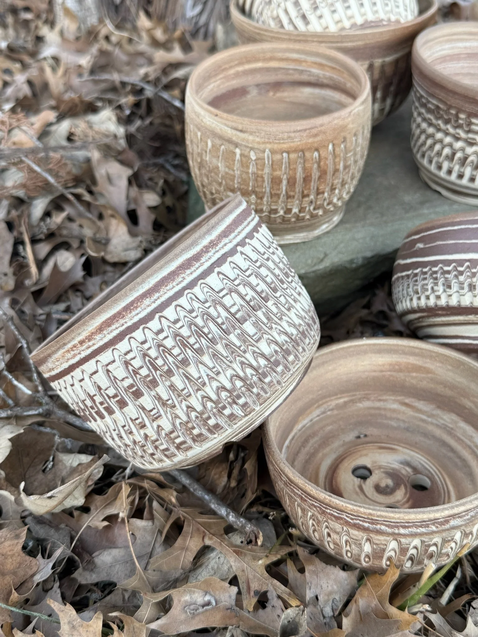 Several round ceramic pots with decorative carved patterns, surrounded by dry fallen leaves.