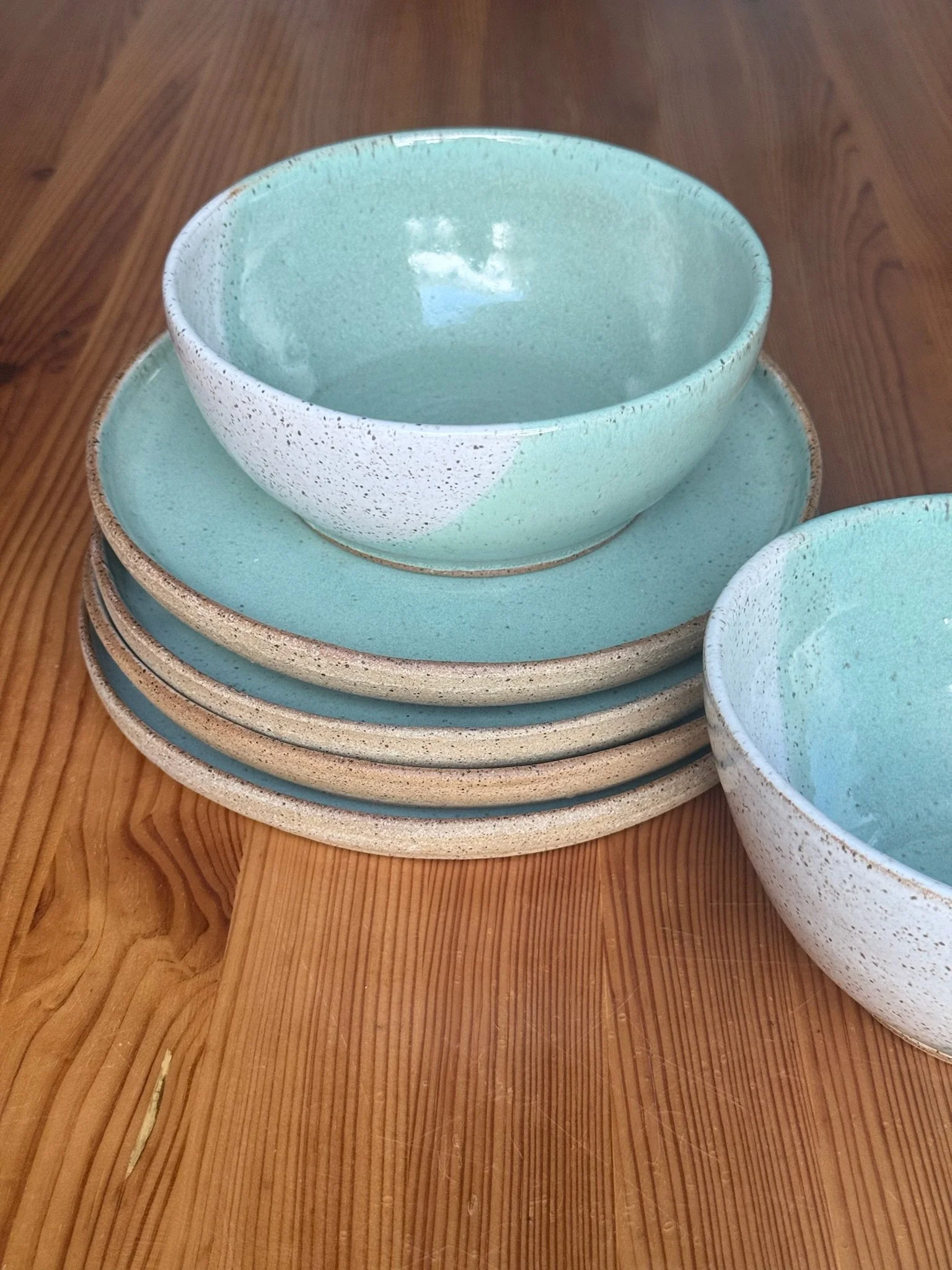 Stacked ceramic bowls and plates in pastel shades of blue and beige on a wooden surface.