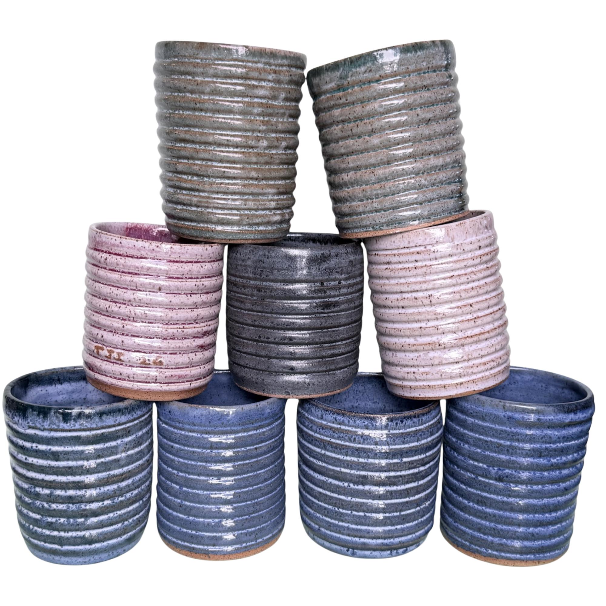 Stack of small ceramic cups with horizontal ridges, in shades of gray, pink, and blue, on a matching plate.