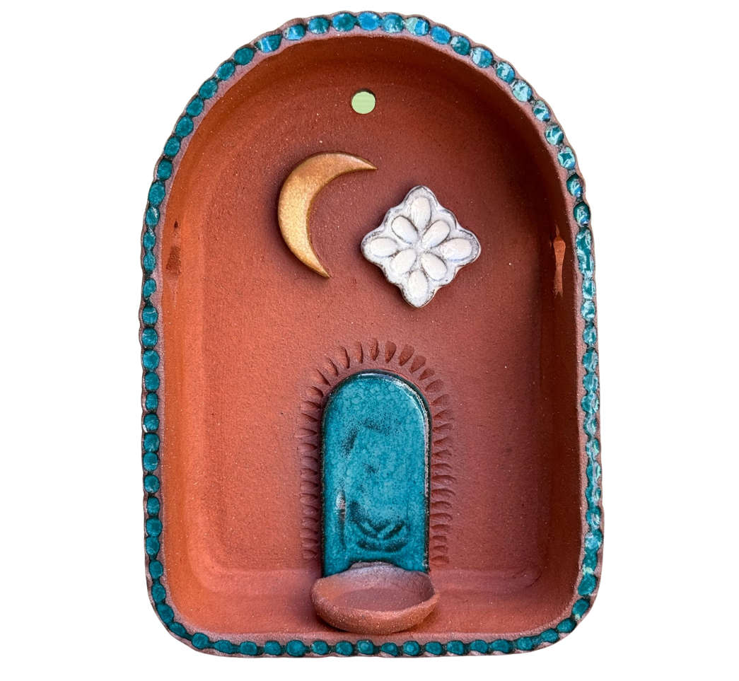 Decorative altar featuring a crescent moon, a white flower, and a blue archway with a small platform in a terracotta-colored niche, outlined with blue beads.