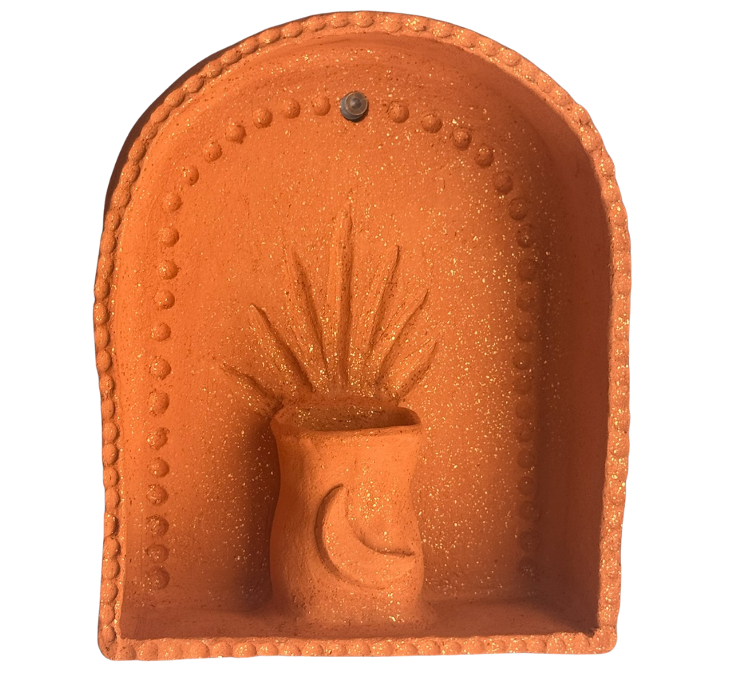 A decorative terracotta wall hanging featuring a cactus in a pot with radiating lines, surrounded by a rounded arched frame with a beaded border.