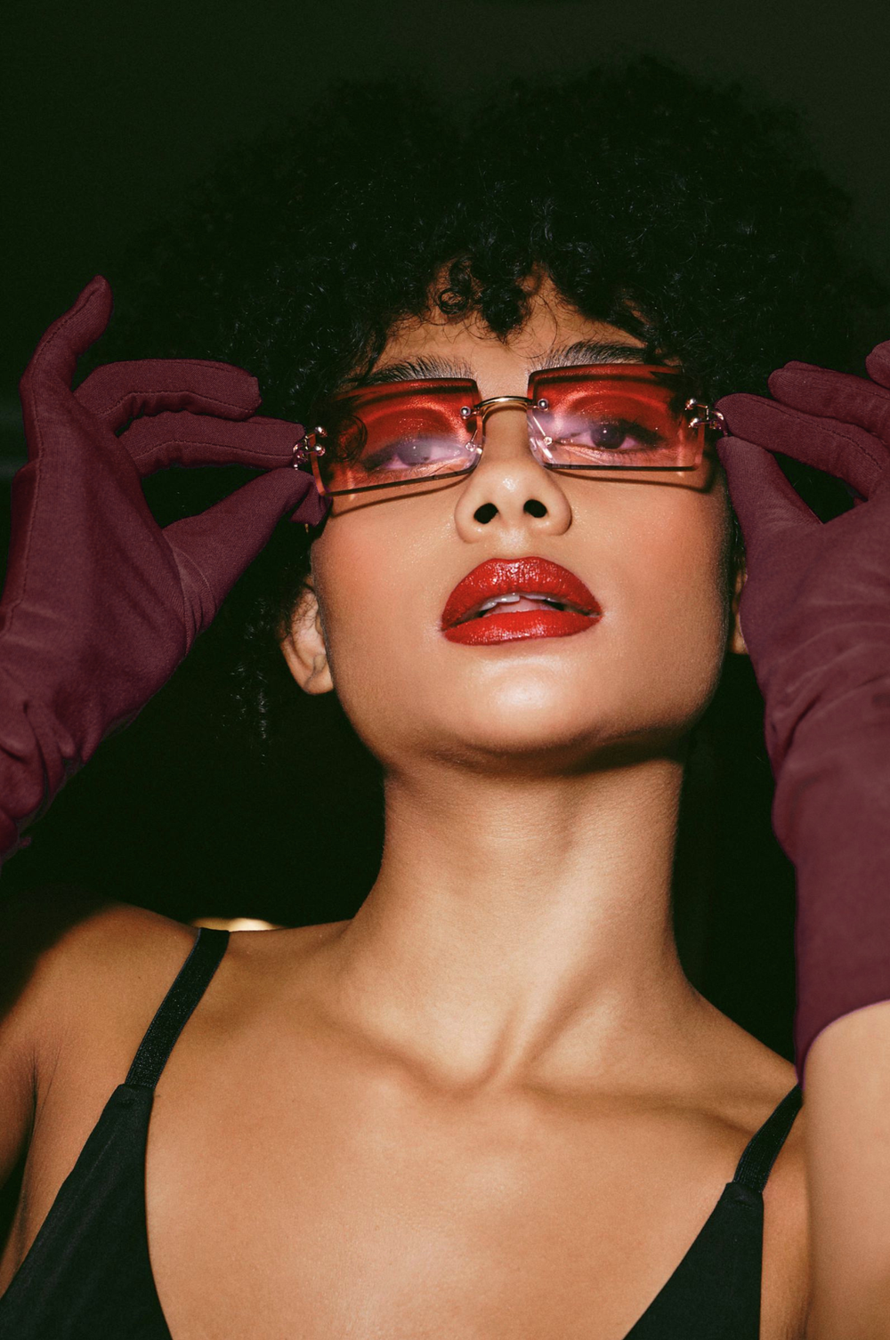 Woman with curly hair in red-tinted glasses and burgundy gloves