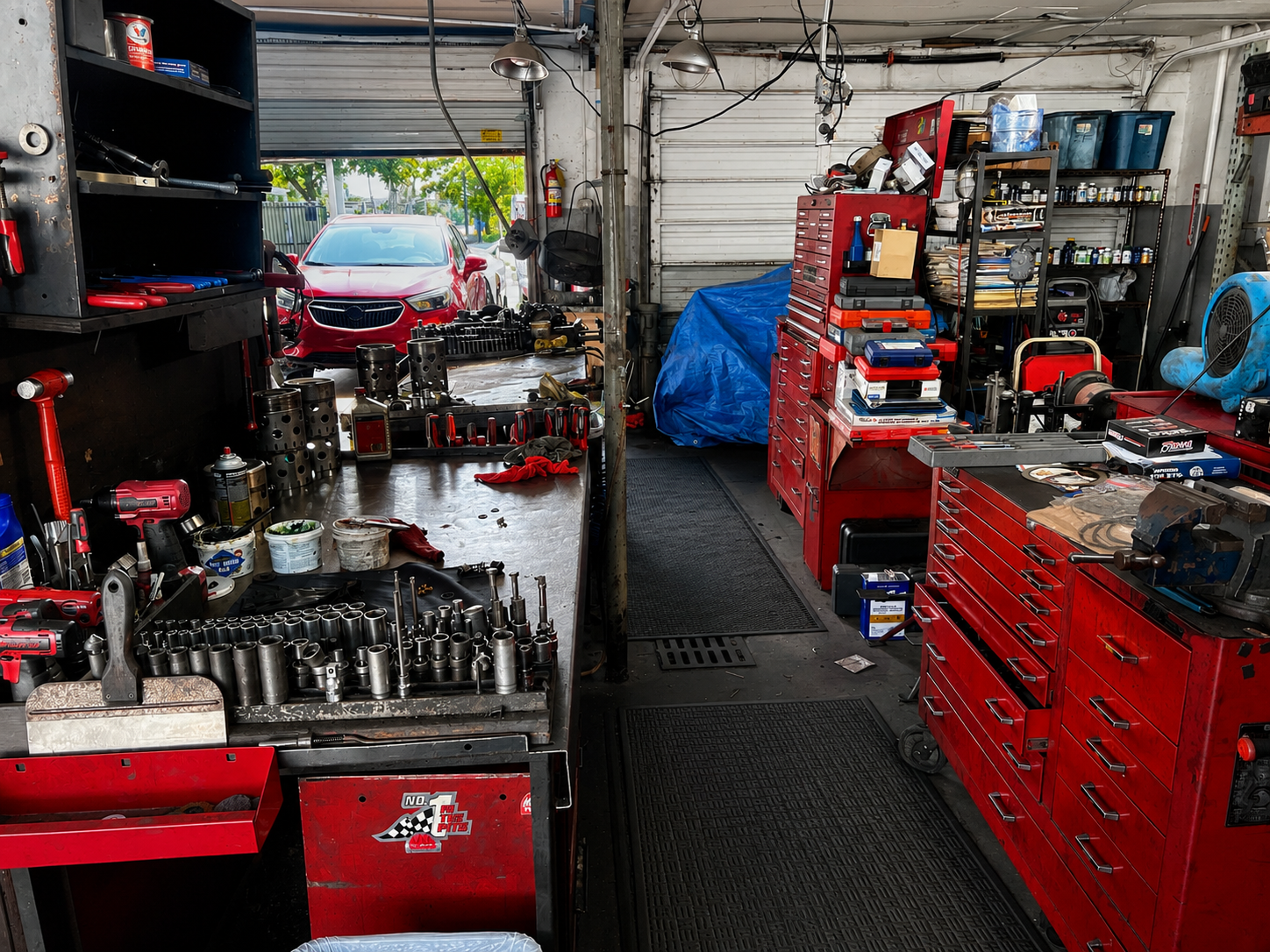 View inside an auto repair shop with red tool cabinets, various tools, and a red car parked outside