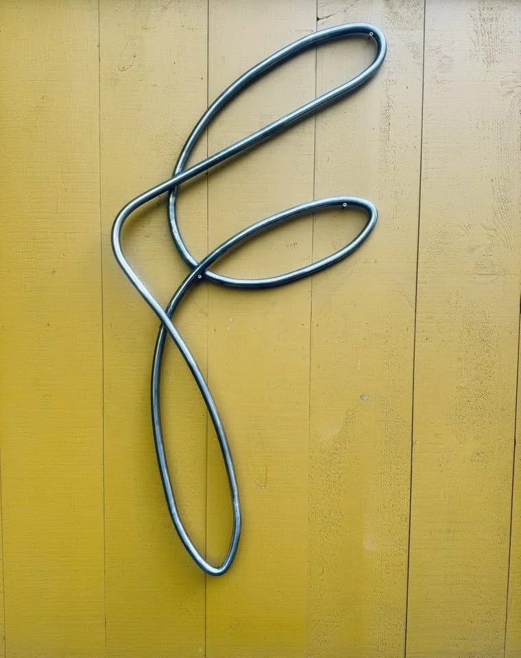 Metal sculpture resembling a stylized flower on a yellow wooden wall.