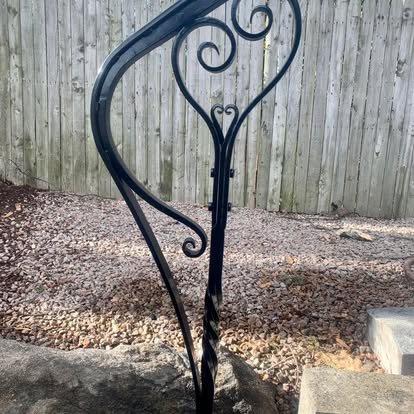 A decorative black wrought iron garden stepladder leaning against a wooden fence.