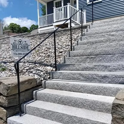 Outside concrete stairs with black metal handrails leading up to a porch with a white railing. A sign for Hillside Euro Works with a phone number is visible near the stairs.
