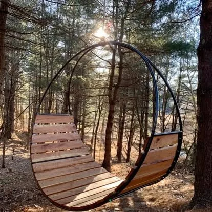 Hand made circular metal and wood swing hanging in a forest with sunlight filtering through trees