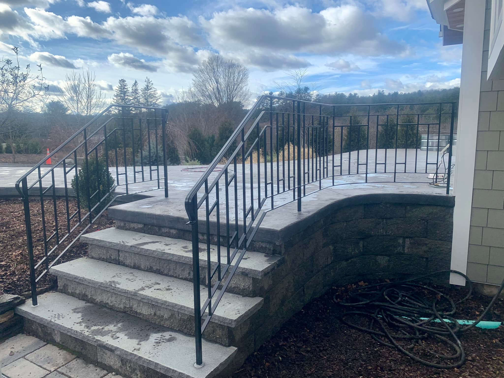 Concrete stairs with black metal railings outside a building, with overcast sky and trees in the background.