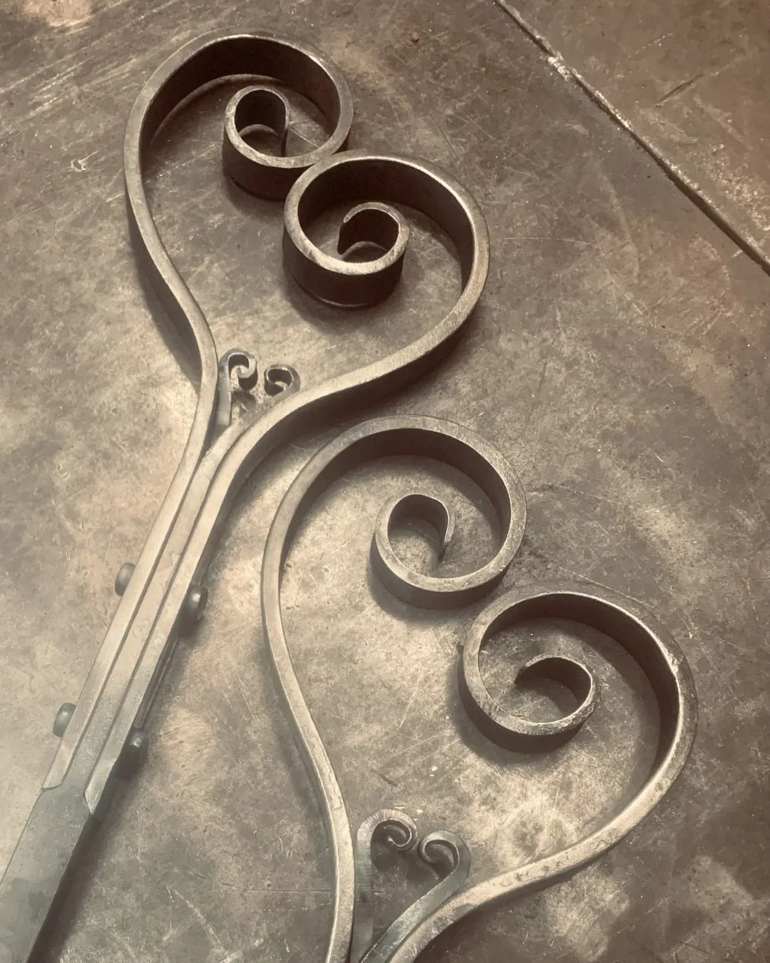 A decorative metal stair railing with intricate swirl designs lying on a concrete floor.