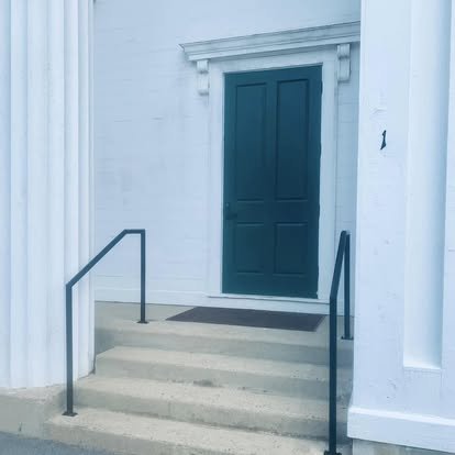 A set of concrete steps with metal railings leading up to a closed teal door on a white building.