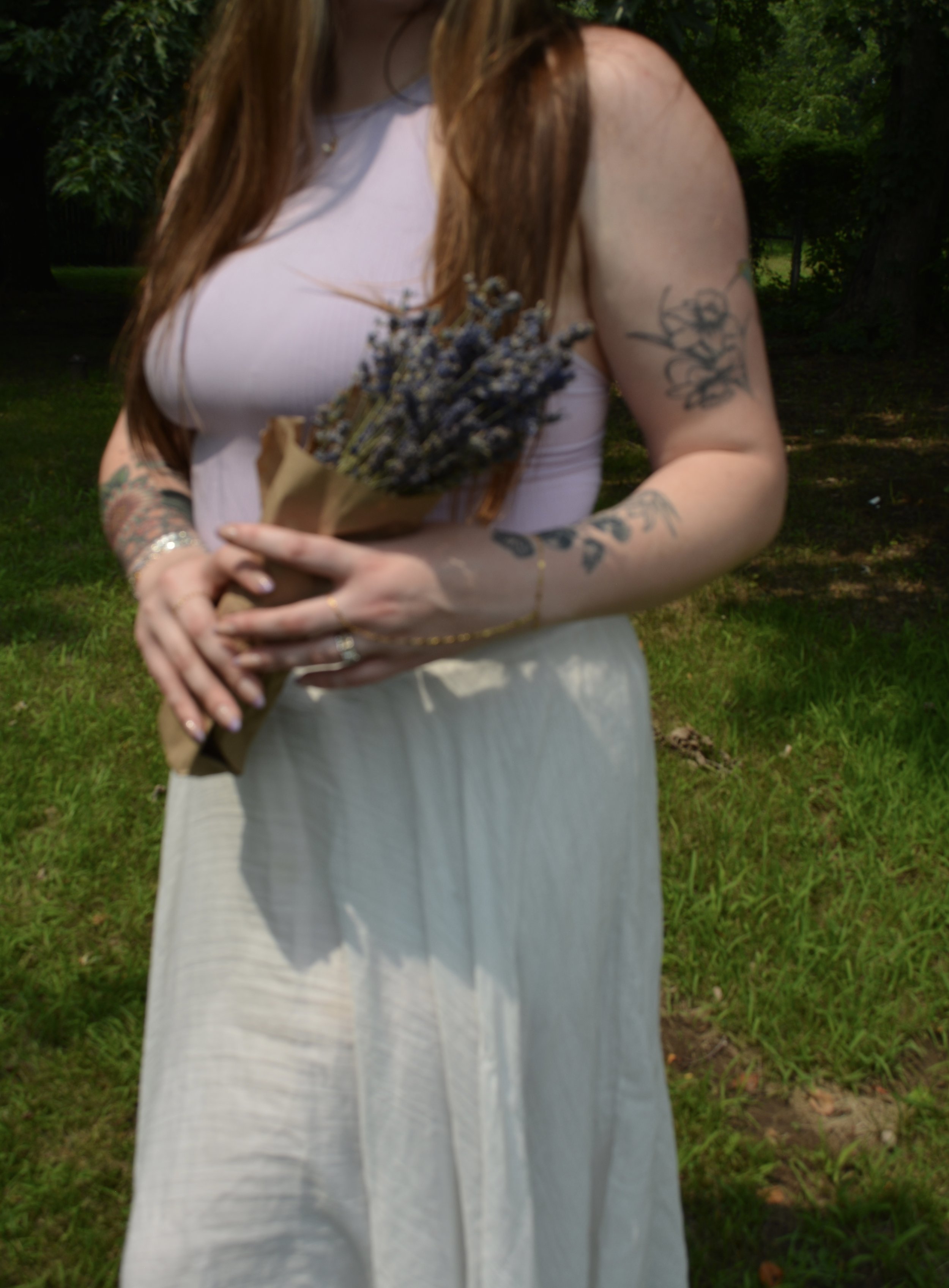 A woman with long auburn hair holding a bouquet of lavender flowers outdoors in a garden or park setting.