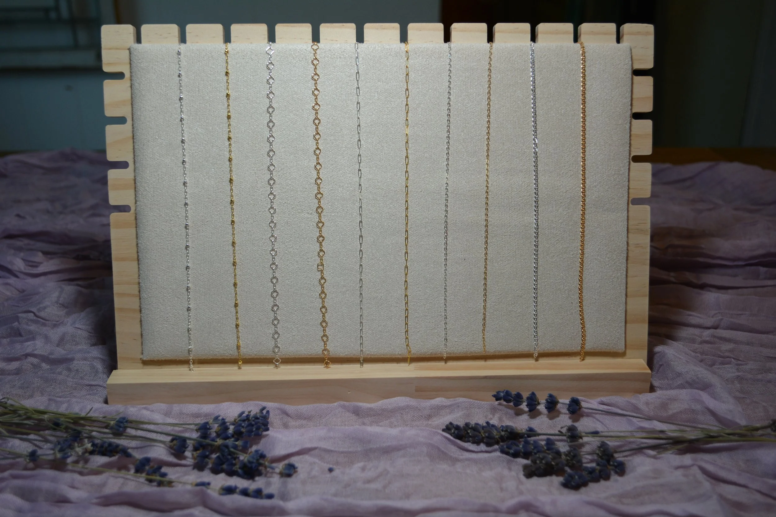 Display of delicate necklaces in silver and gold on a jewelry stand, surrounded by purple flowers.