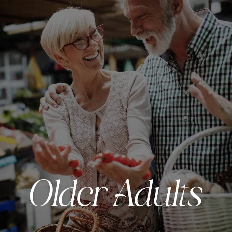 Smiling elderly woman and man shopping at a farmers market or grocery store, holding strawberries and smiling at each other.