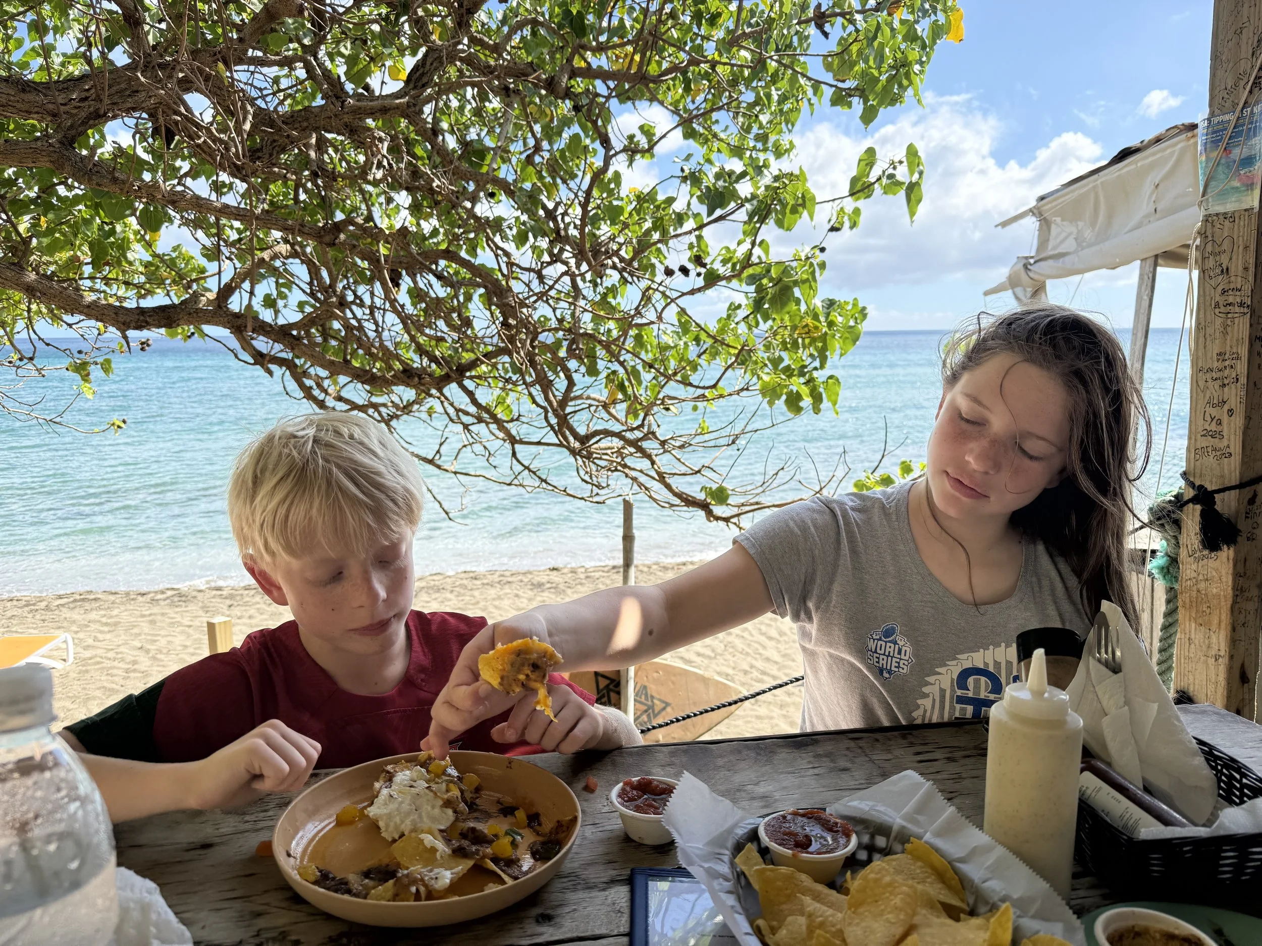 A young boy and young woman eating breakfast by a beach, with a teal blue ocean behind them.
