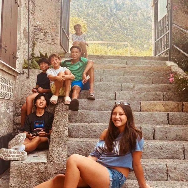 A group of five preteens hanging out on a set of stone steps, with an adult posed behind them at the top of the steps.