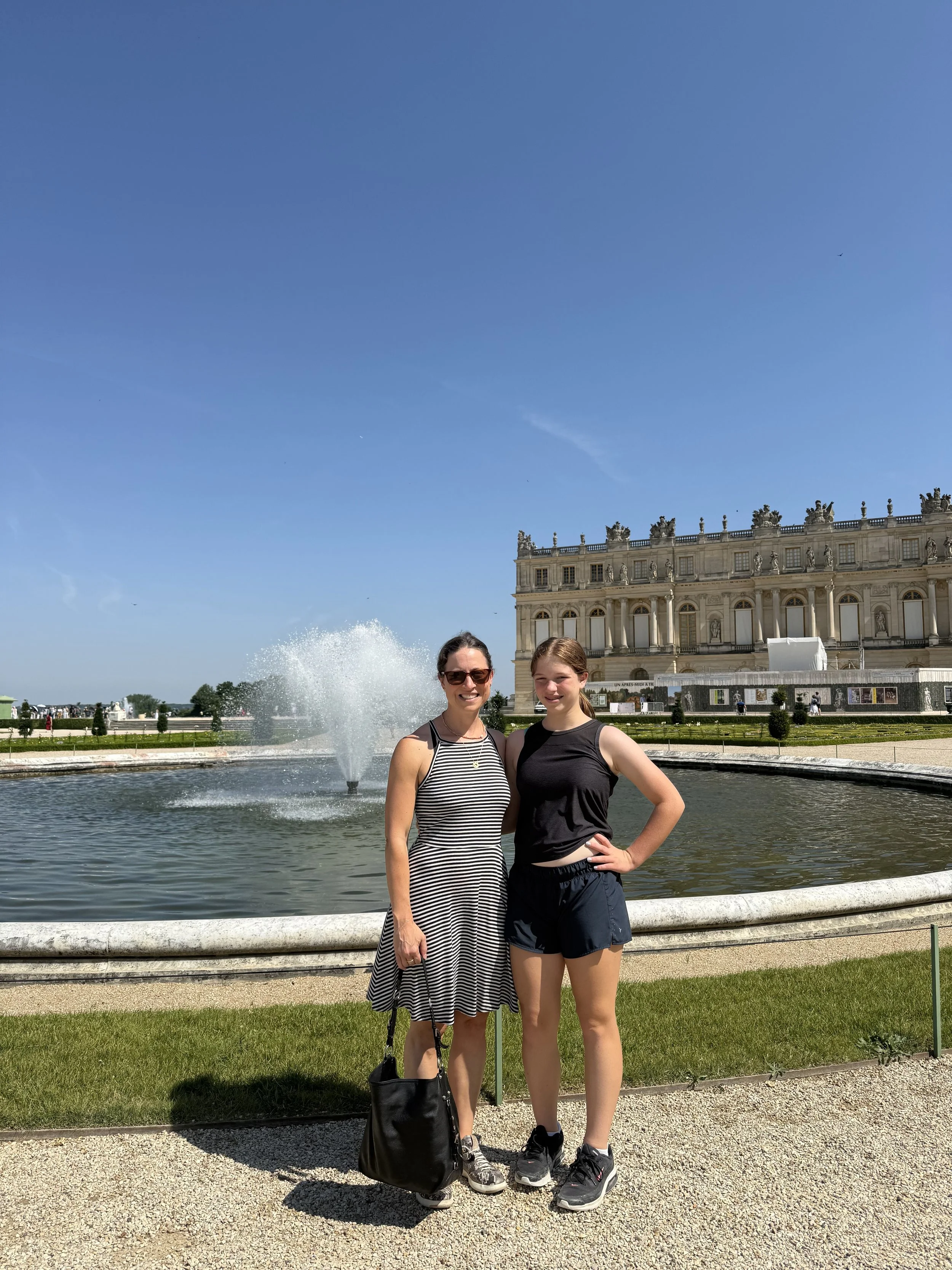 A mother and daughter on a sunny day smiling and standing in front of a fountain at Versailles