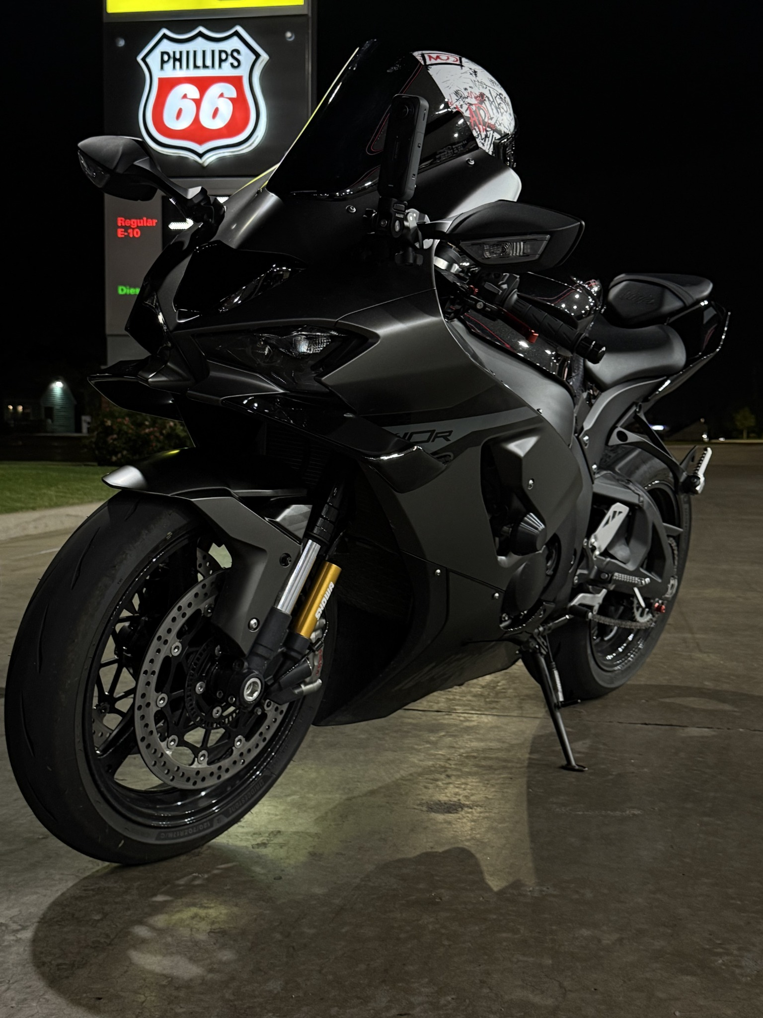 Black and gray sport motorcycle parked at night in front of a Phillips 66 gas station sign