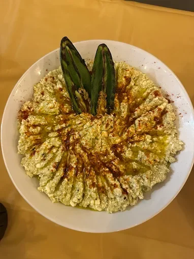 A white bowl filled with a creamy dish, topped with two grilled green chili peppers and drizzled with a dark sauce.