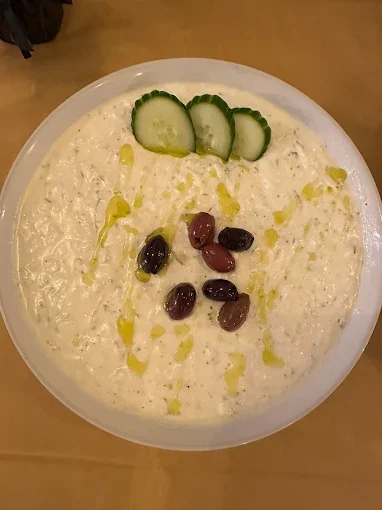 A bowl of creamy white yogurt garnished with sliced cucumbers, a drizzle of olive oil, and a few olives.