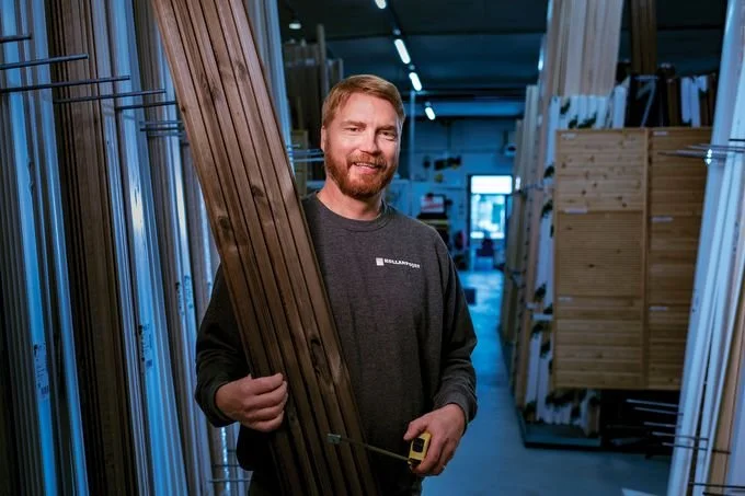 KollanPoikien Max-Johan pitää kädessään lautaa ja mittanauhaa, ja hymyilee kameralle.