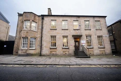 A historic stone building with multiple windows and a centered entrance, located on a city street.