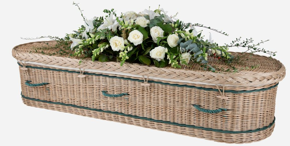 Rattan coffin with white and green floral arrangement on top