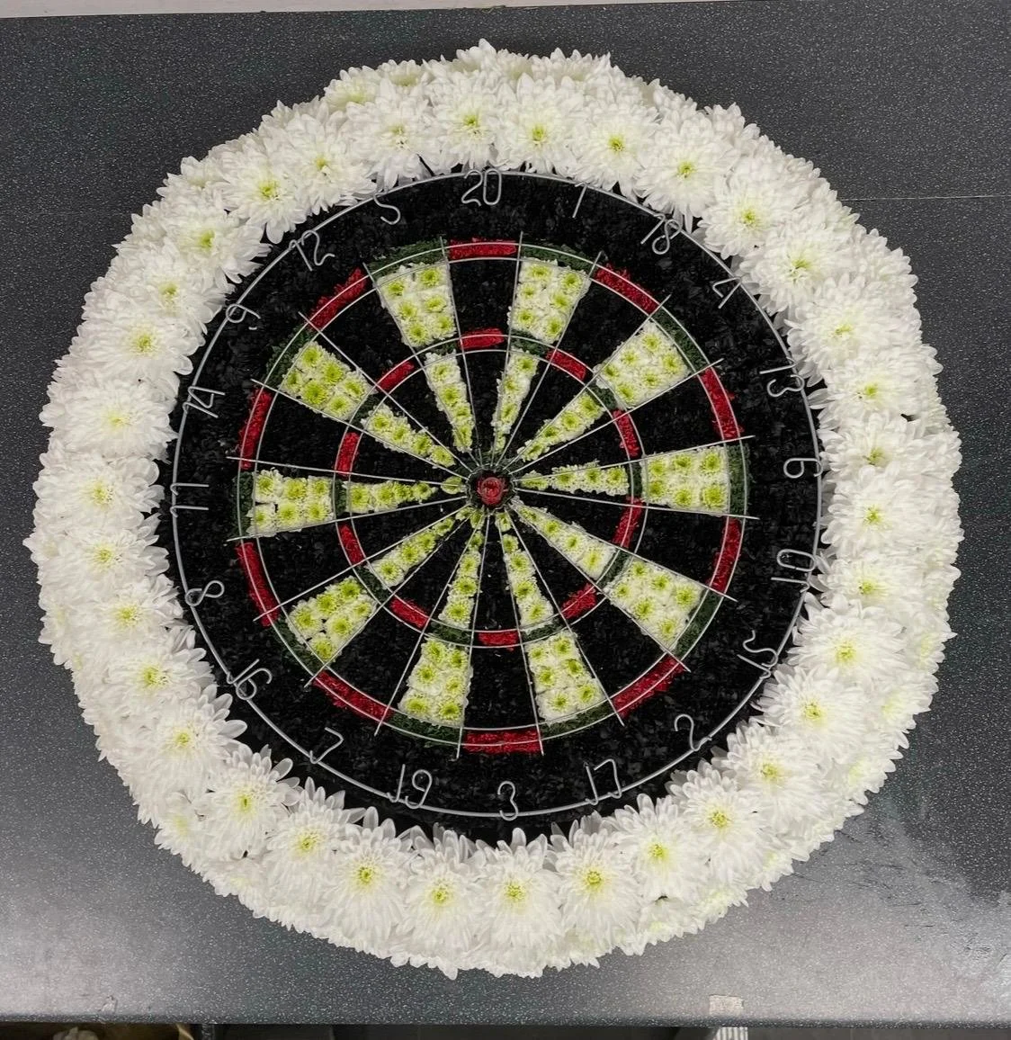 A decorative dartboard surrounded by white flowers on a dark surface.