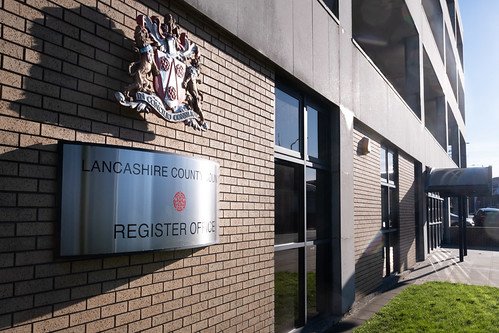 Exterior of a Lancashire County Register of Deeds building with a coat of arms and a sign on a brick wall.